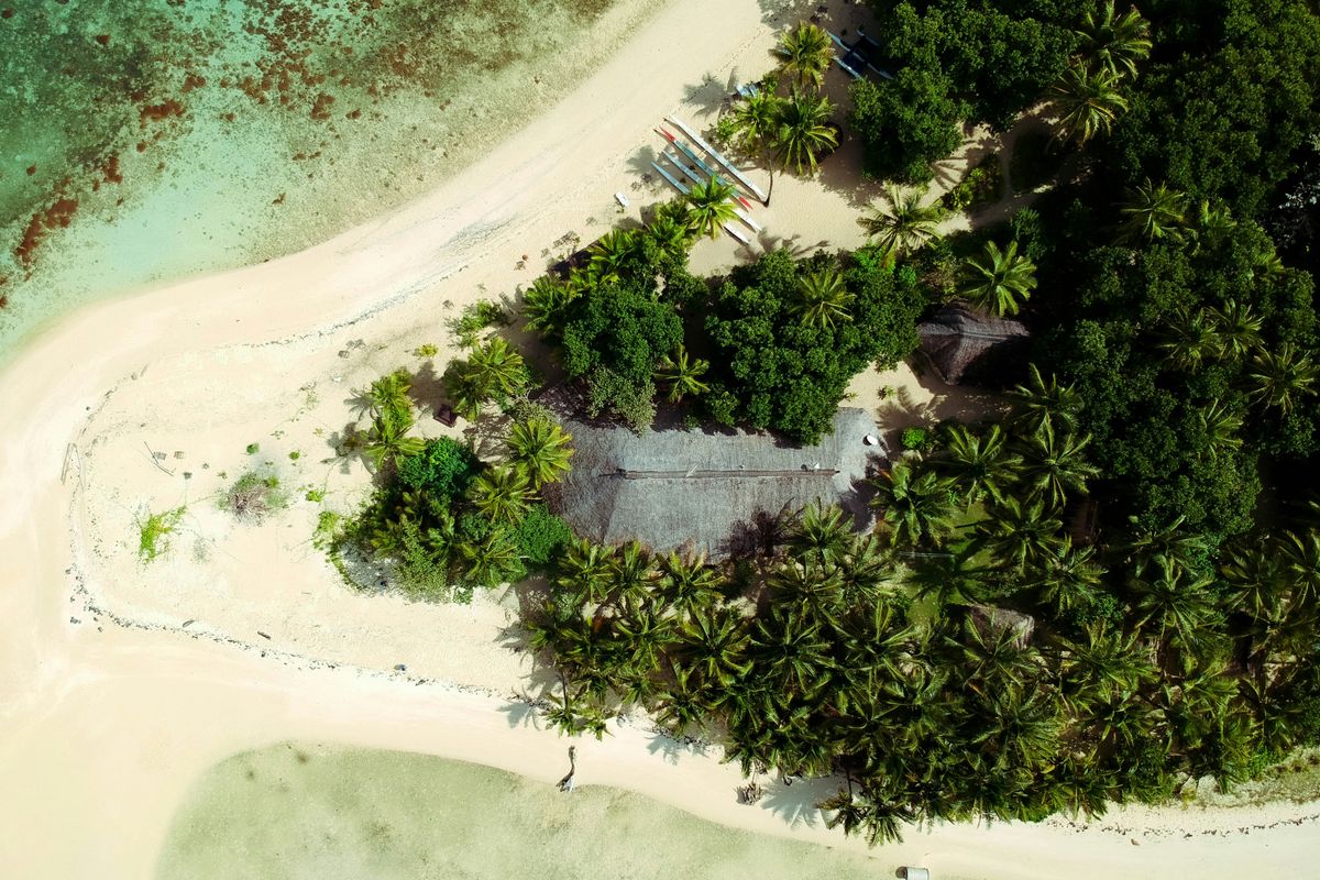 Aerial view of a secluded palm-fringed sandbar and turquoise lagoon on a Fijian island.